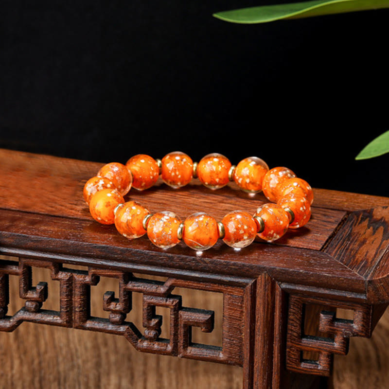 Oranges Perlenarmband mit Metallperlen auf Holzständer.