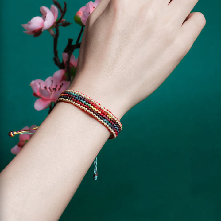 Tibetisches Armband Regenbogen bunt geflochten am Handgelenk mit rosa Blüten