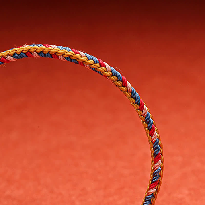 Geflochtenes Armband mit roten, gelben und blauen Schnüren vor rotem Hintergrund Nahaufnahme