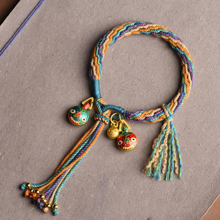 Buntes Armband mit Glücksvögeln und goldenen Anhängern auf Leinen.