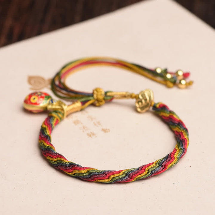 Buntes Seiden-Armband mit goldenen Charms auf weißem Hintergrund.