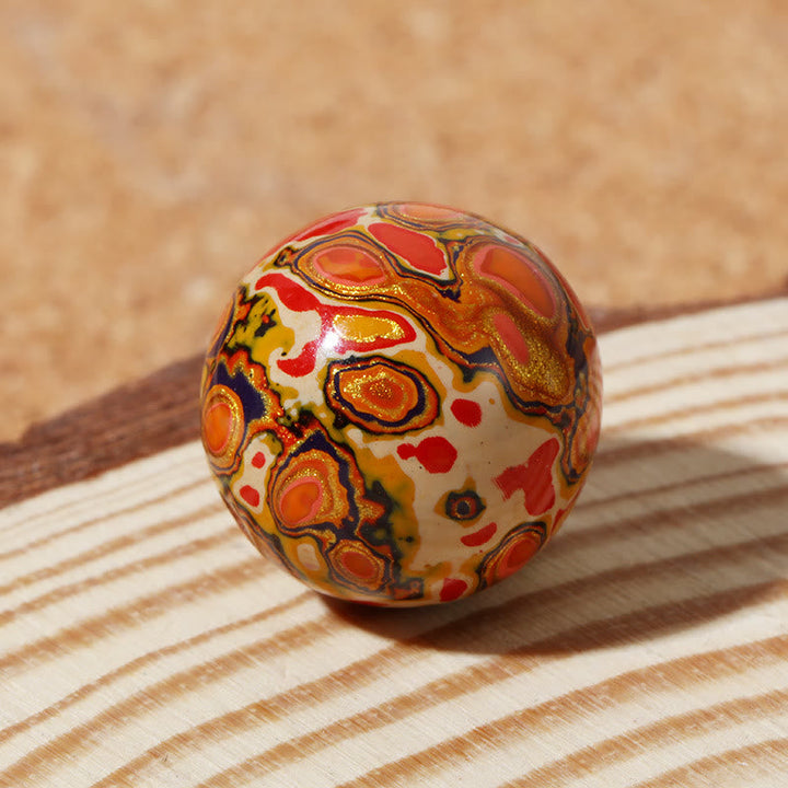 Bunte lackierte Perle mit orangeroten Mustern auf Holzoberfläche.