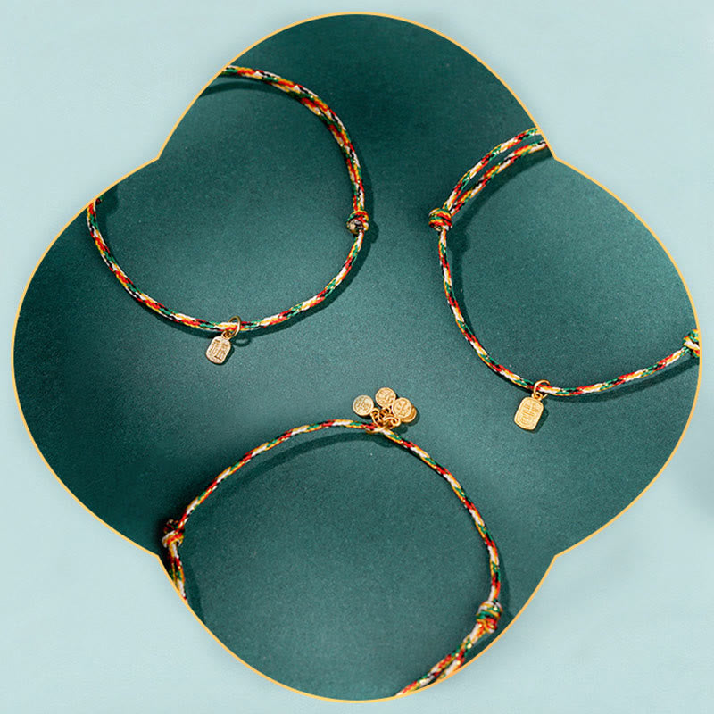 Drei bunte Armbänder mit Fu-Zeichen Anhängern auf grünem Tablett.