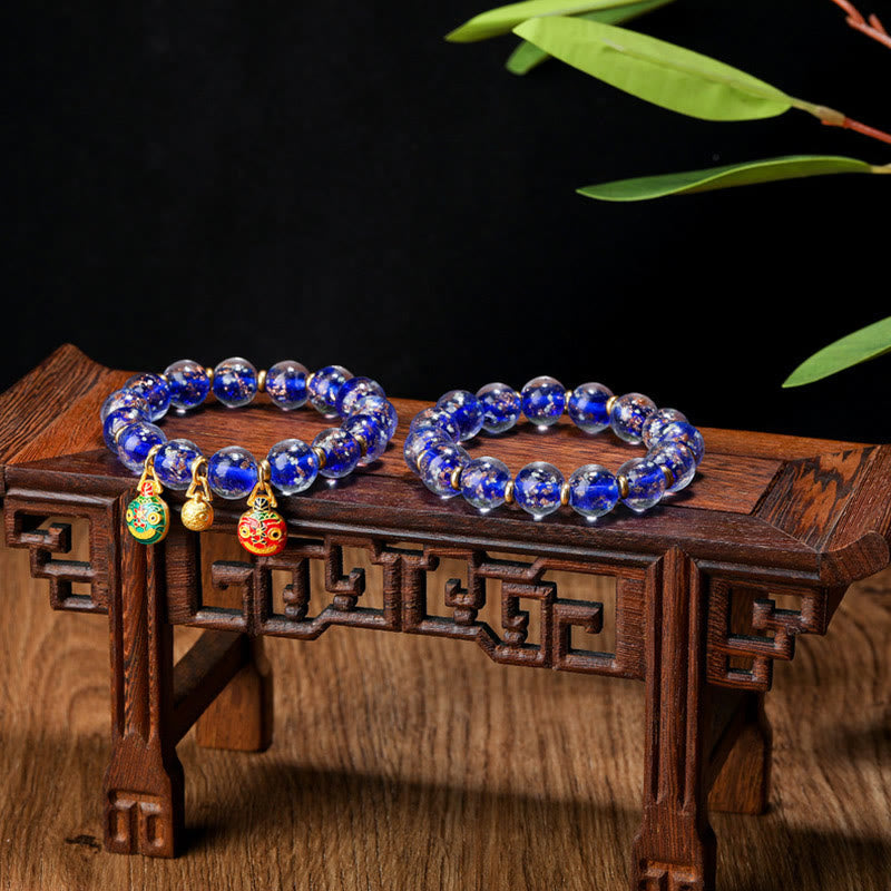 Blaues Lapislazuli Armband mit goldenen Anhängern auf Holzständer.
