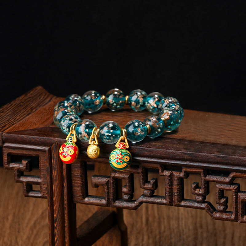 Grünes Kristallarmband mit goldenen Glücksbringern auf Holztisch.
