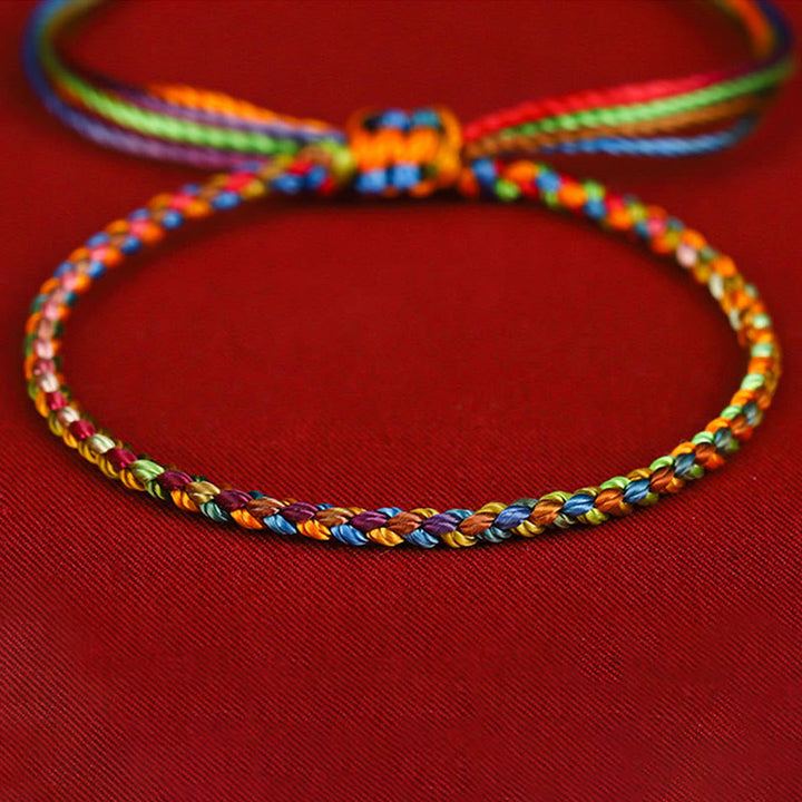 Buntes Glücksarmband mit Regenbogenfäden auf rotem Hintergrund, Nahaufnahme