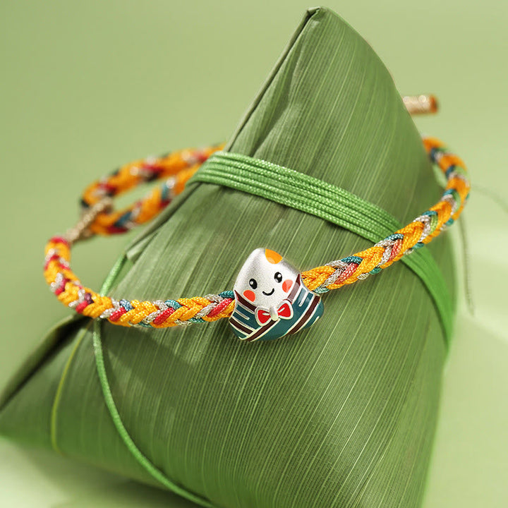 Farbenfrohes Glücksarmband mit süßem Daruma-Anhänger auf grünem Blatt.