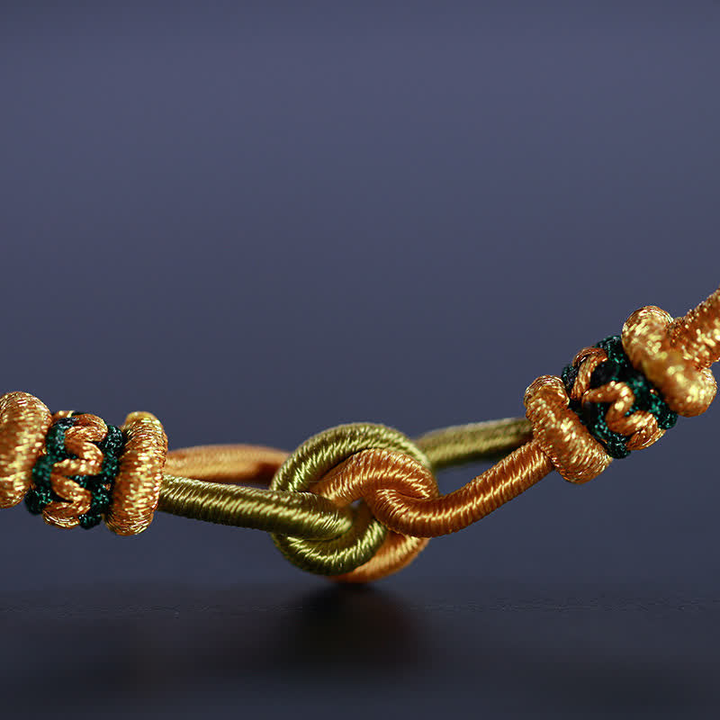 Goldfarbenes geflochtenes Armband mit Knoten Details vor grauem Hintergrund.