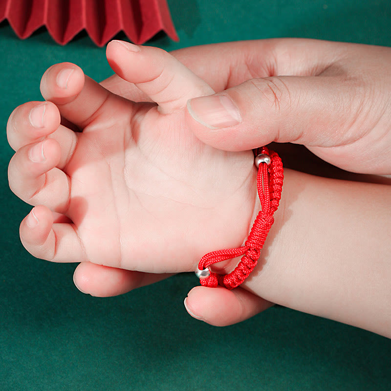 Rotes Armband Glück Tierkreis Babyhände Grüner Hintergrund elastisch.