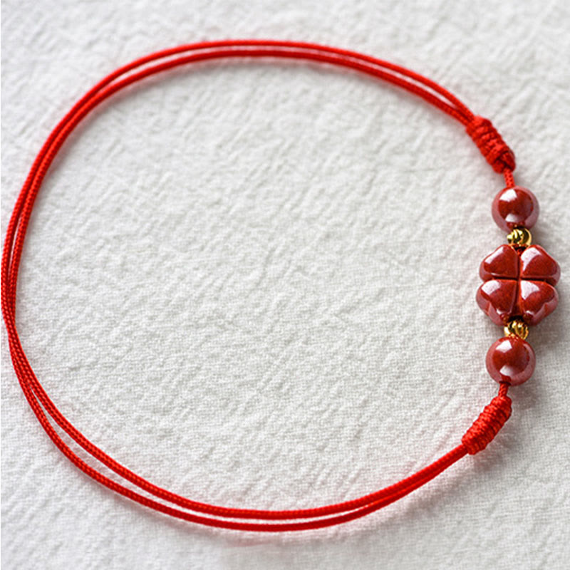 Rotes Armband Zinnober Kleeblatt mit goldenen Perlen, Flachaufnahme Textilhintergrund