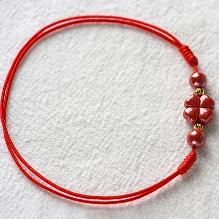 Rotes Armband Zinnober Kleeblatt mit goldenen Perlen, Flachaufnahme Textilhintergrund