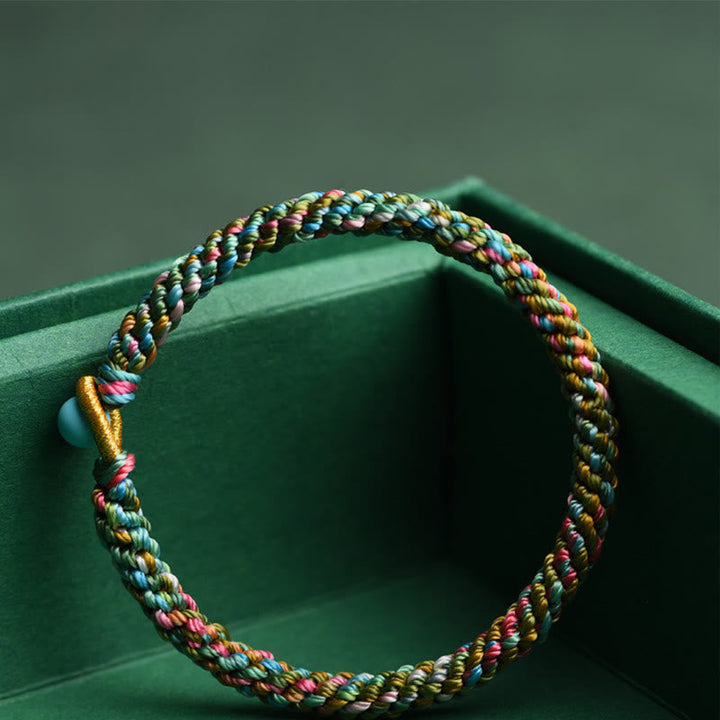 Buntes geflochtenes Armband Glück auf grünem Hintergrund getragen.
