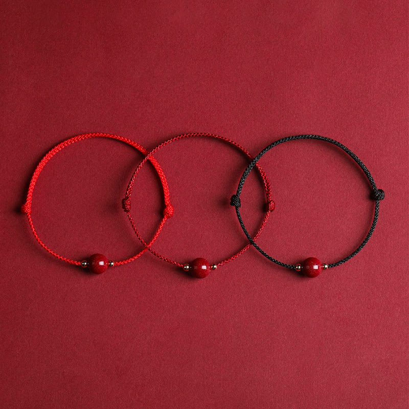 Drei rote Armbänder Zinnober – Glück & Segen auf rotem Hintergrund Flachlage