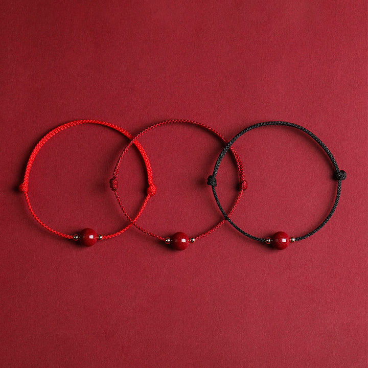 Drei rote Armbänder Zinnober – Glück & Segen auf rotem Hintergrund Flachlage