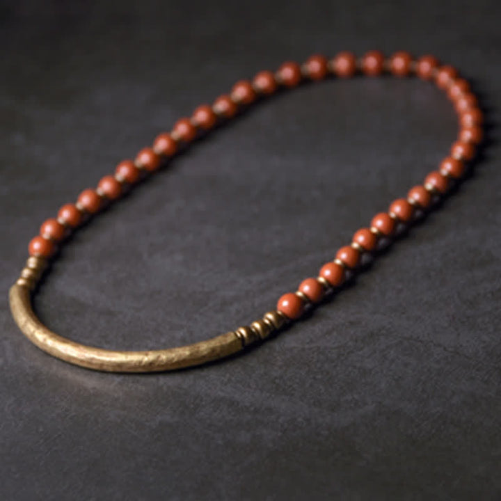 Armband mit roten Perlen und bronzefarbenem Verschluss auf dunklem Hintergrund.