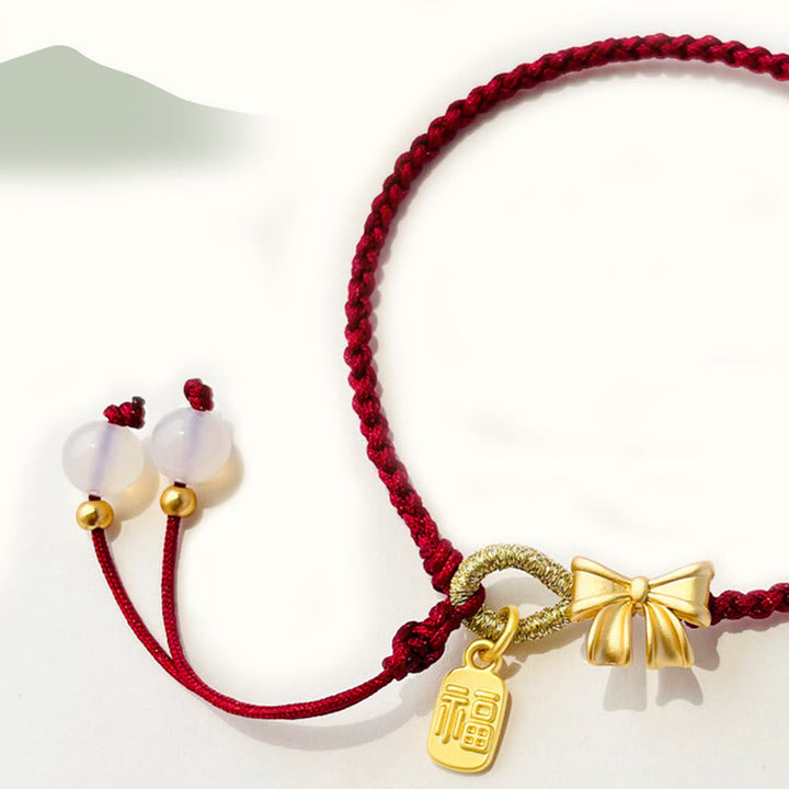Rotes Armband Pfirsichblüte mit goldenen Anhängern elegant präsentiert.