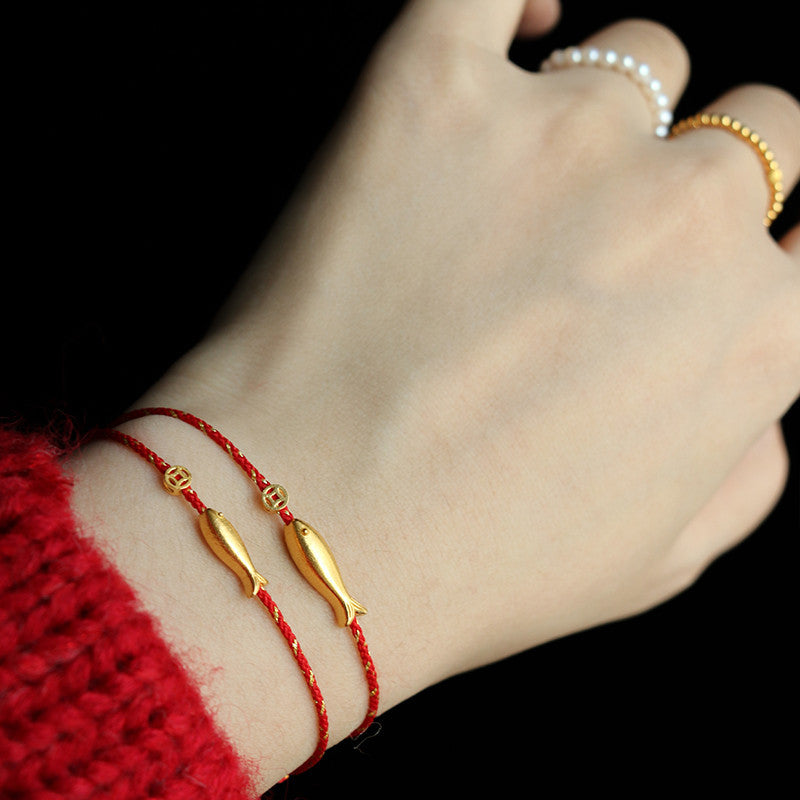 Rote Armbänder mit goldenen Koi-Fisch-Anhängern am Handgelenk getragen.