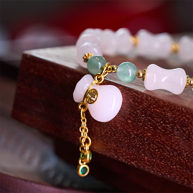 Jade Armband mit rosa Steinen und goldenen Elementen auf Holz.