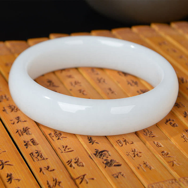 Weißes Jade Armband auf Holz mit chinesischen Schriftzeichen Glück Wohlstand Segen