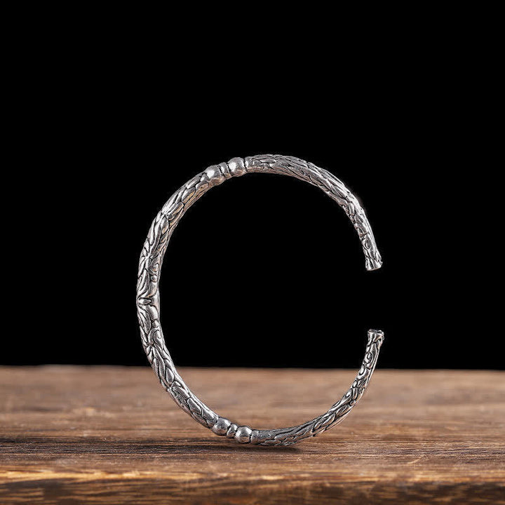 Silbernes Drachen-Armband mit strukturiertem Design auf Holzoberfläche.