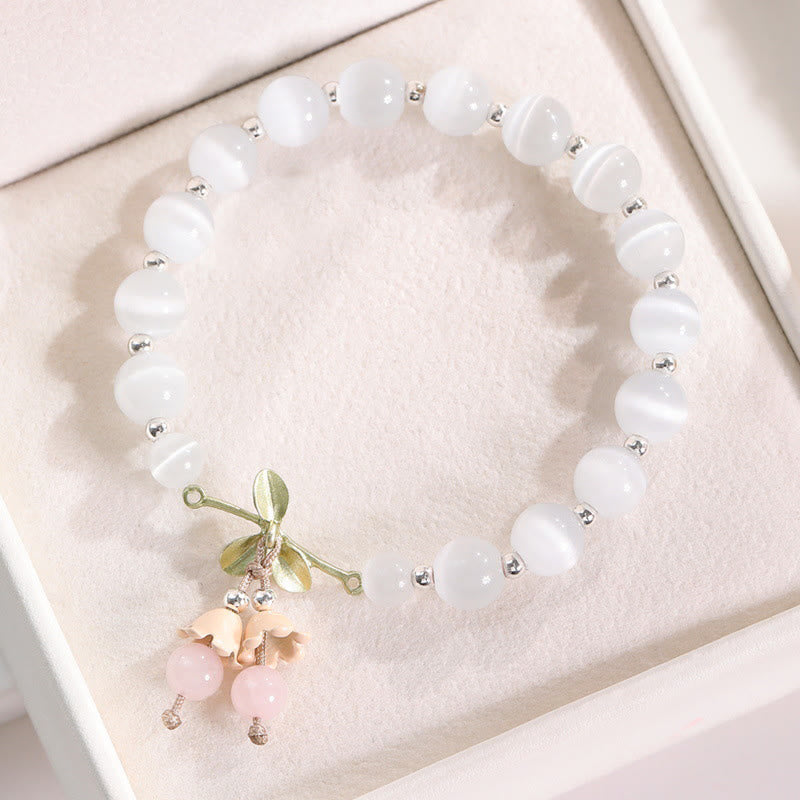 Weißes Perlenarmband mit rosa Katzen-Charm auf Stoffhintergrund.