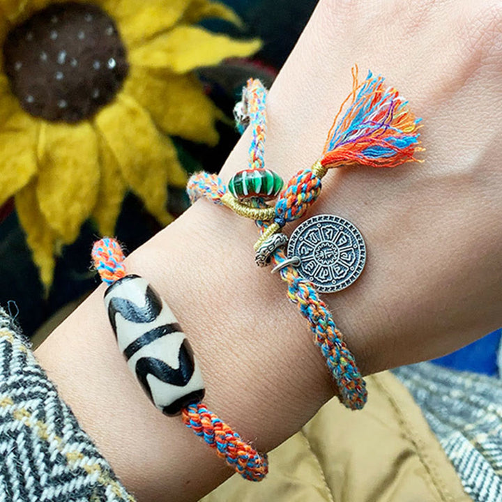 Bunte Armbänder mit Om-Symbol und Quaste am Handgelenk getragen.