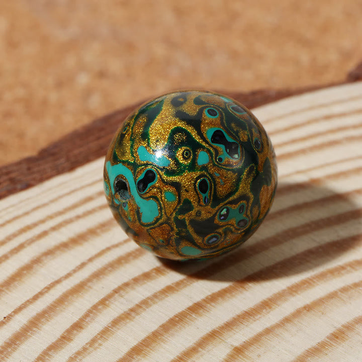 Bunte Lacquer Perle mit türkis-gold Muster auf Holzoberfläche.