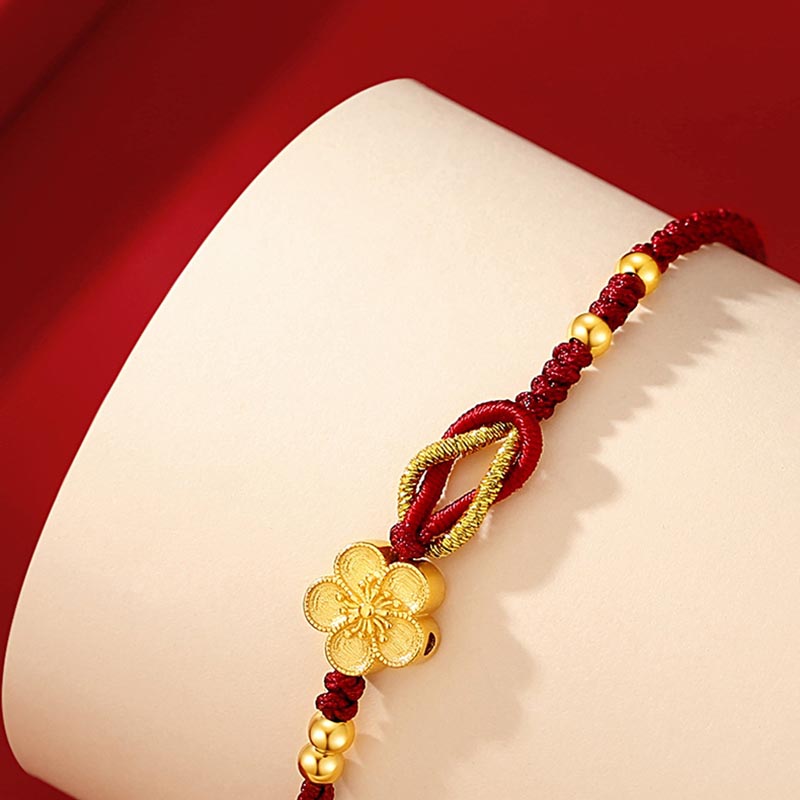 Rotes Seidenarmband mit goldenem Blütenanhänger und Perlen elegant.