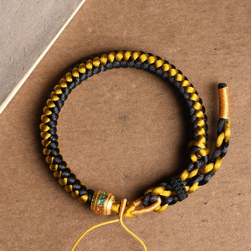Geflochtenes Armband Om Mani Padme Hum Gold Schwarz Handgelenk getragen.