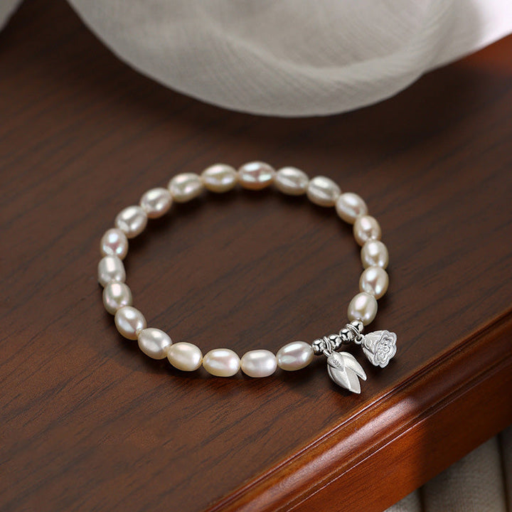 Elegantes Perlenarmband mit Silber Lotus Charm auf Holztisch.