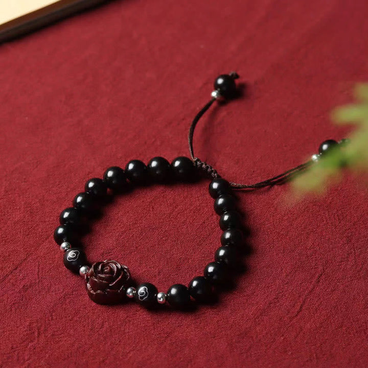 Schwarzes Perlen Armband mit Sandelholz Rose auf rotem Hintergrund.