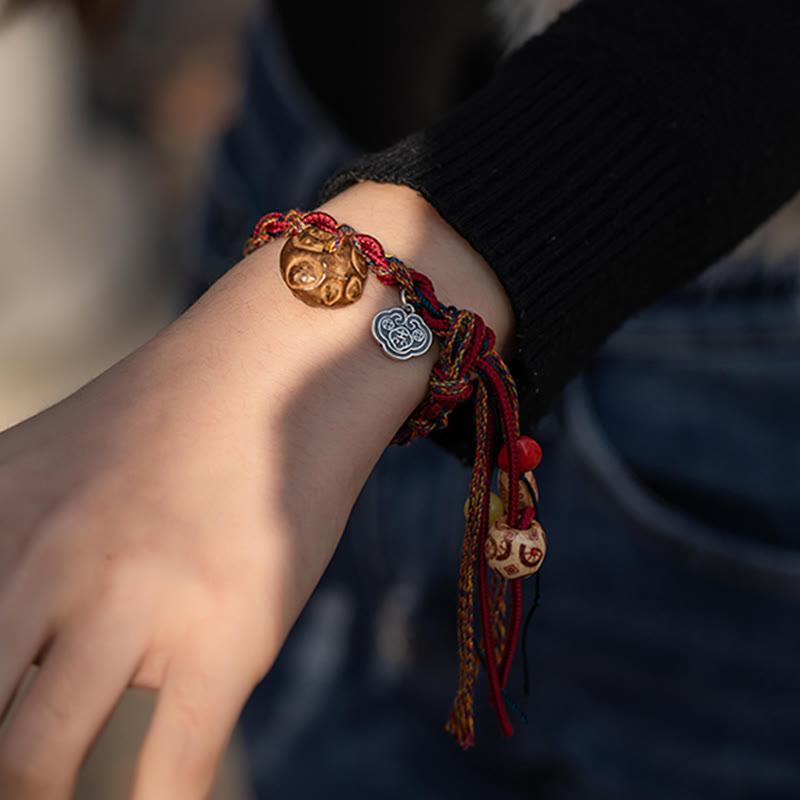 Rotes Armband mit goldenen und silbernen Fisch-Anhängern am Handgelenk.