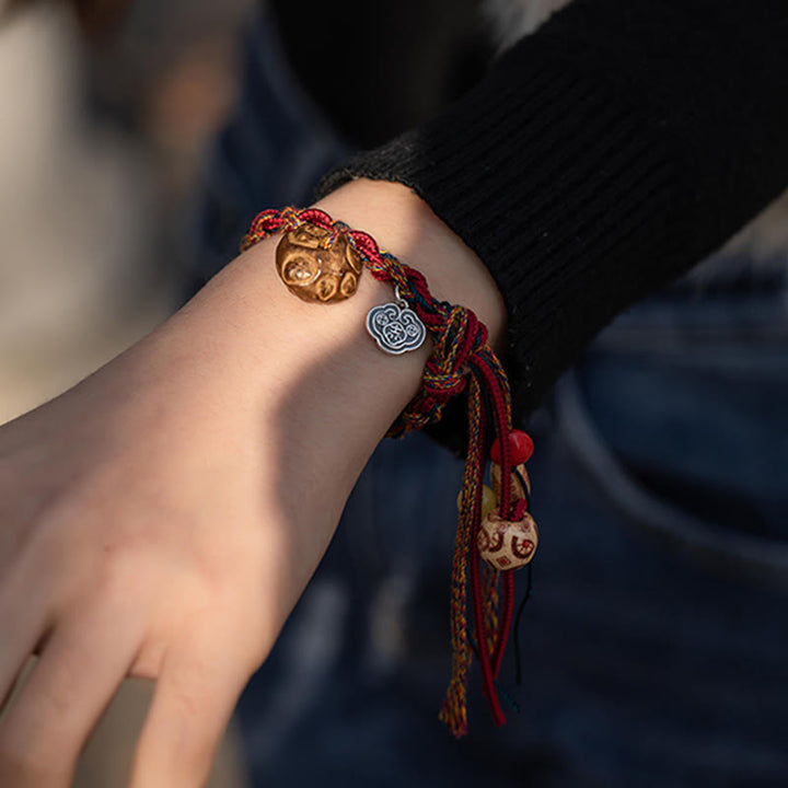 Rotes Armband mit goldenen und silbernen Fisch-Anhängern am Handgelenk.