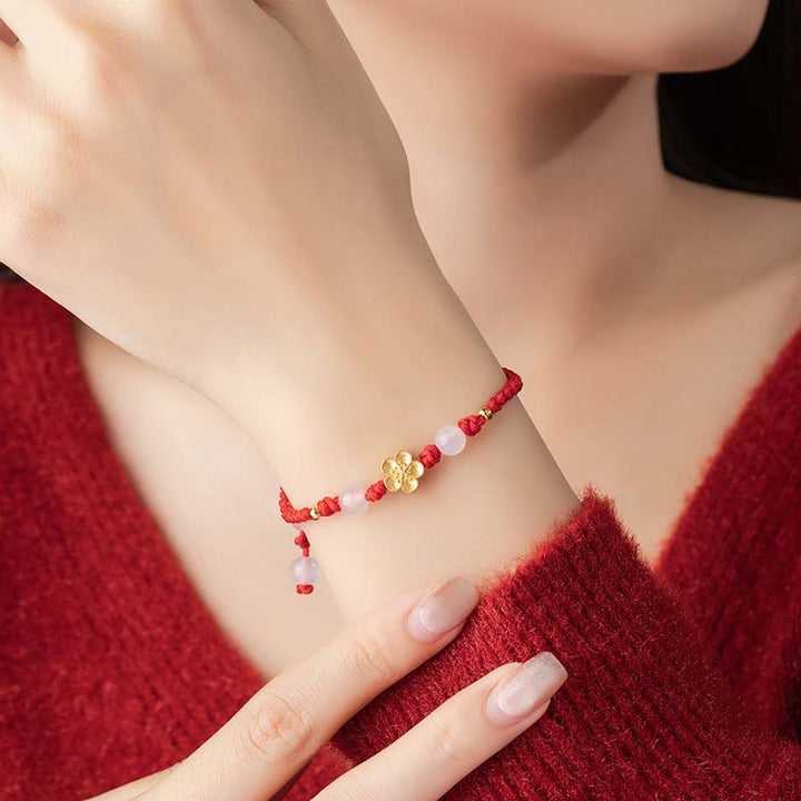 Rotes Armband mit Pfirsichblüte Charm am Handgelenk getragen elegant.
