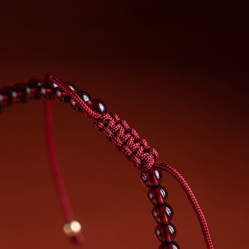 Rotes Armband mit Granatperlen und gewebtem Design, elegant drapiert.