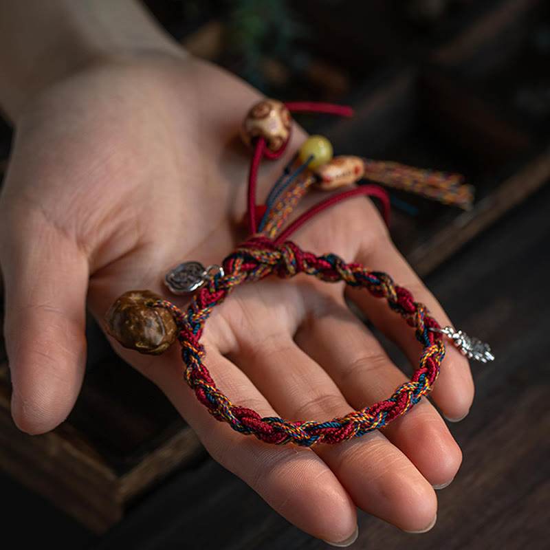Rotes Armband mit Koi-Fisch-Anhänger am Handgelenk, Schutz und Stärke symbolisierend.