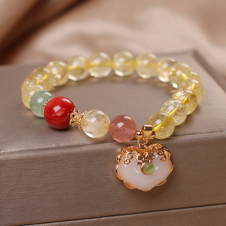 Armband mit Erdbeerquarz, Weiße Jade und goldenen Verzierungen auf Holzoberfläche.