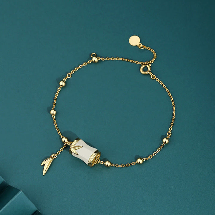 Goldenes Armband mit weißer Jade und Bambus-Anhängern auf Türkis.