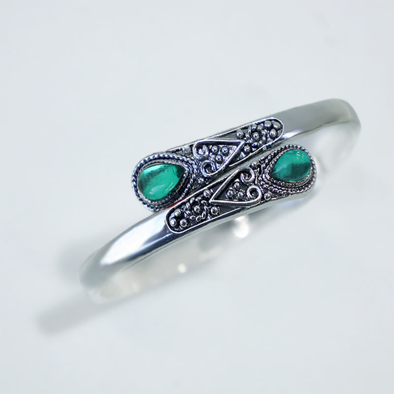 Silbernes Armband mit grünen Steinen und Ornamenten auf weißem Hintergrund