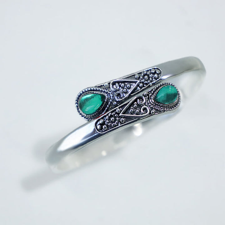 Silbernes Armband mit grünen Steinen und Ornamenten auf weißem Hintergrund