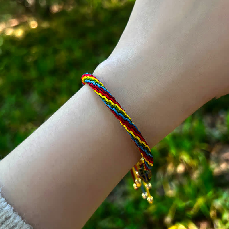 Regenbogenfarbenes geflochtenes Armband mit Goldperlen am Handgelenk getragen.