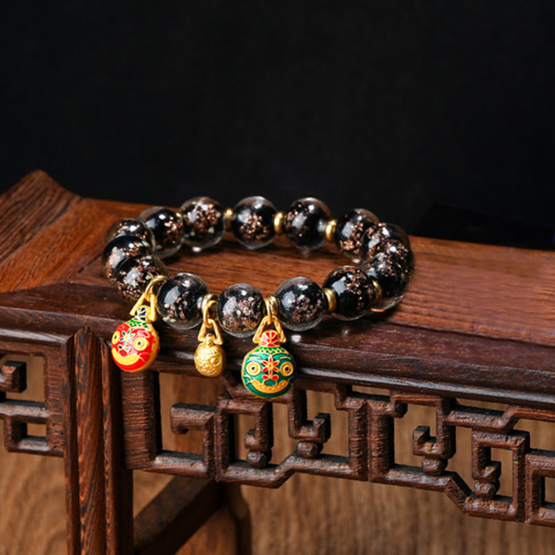 Schwarzes Obsidian Pixiu Armband mit vergoldeten Charms auf Holz.