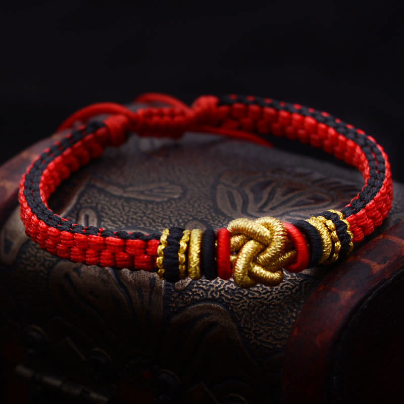 Rotes Armband – Glück & Liebe mit goldenen Verzierungen auf Holz.