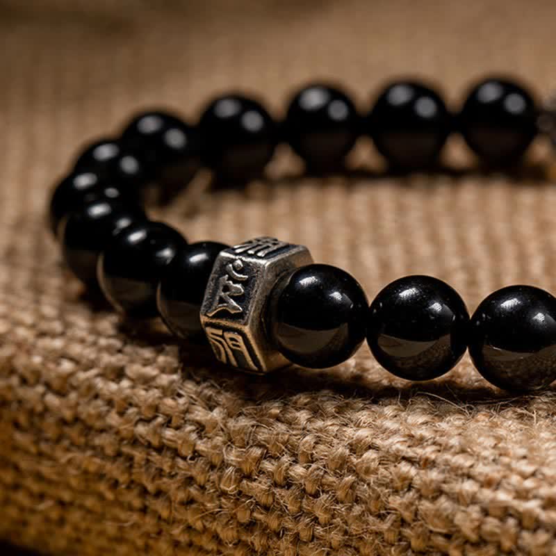 Schwarzes Obsidian Armband mit verziertem Silbermetall-Element auf Leinen.