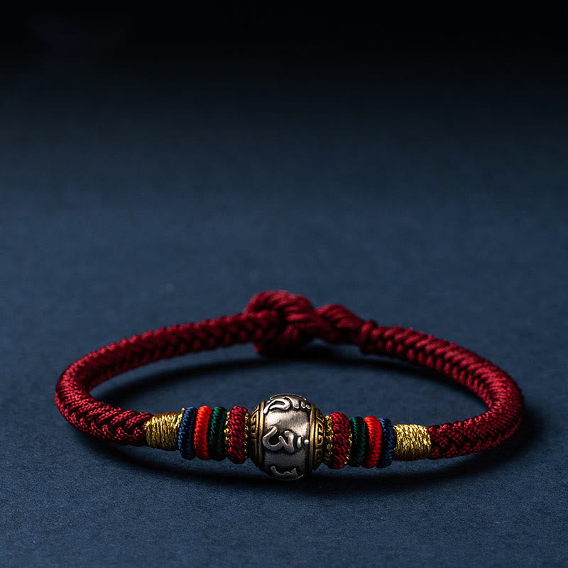 Rotes Armband mit silbernem Om-Anhänger auf dunkelblauem Hintergrund elegant präsentiert.