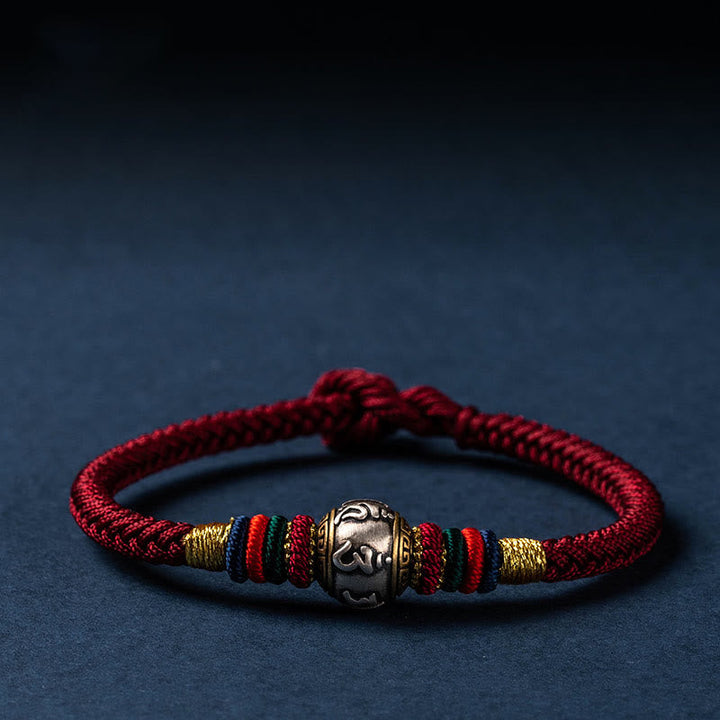 Rotes Armband mit silbernem Om-Anhänger auf dunkelblauem Hintergrund elegant präsentiert.