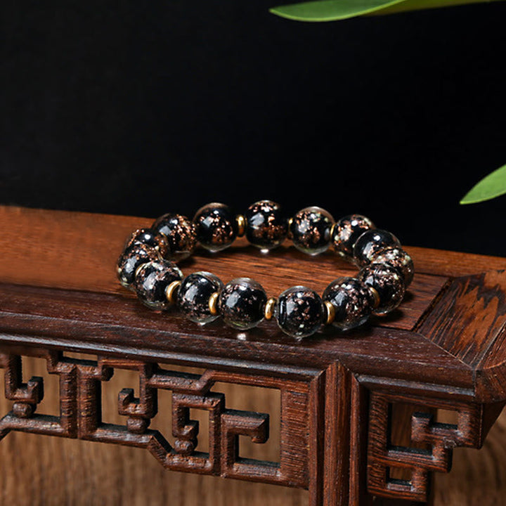 Schwarzes Obsidian Pixiu Armband mit Goldakzenten auf Holzoberfläche.