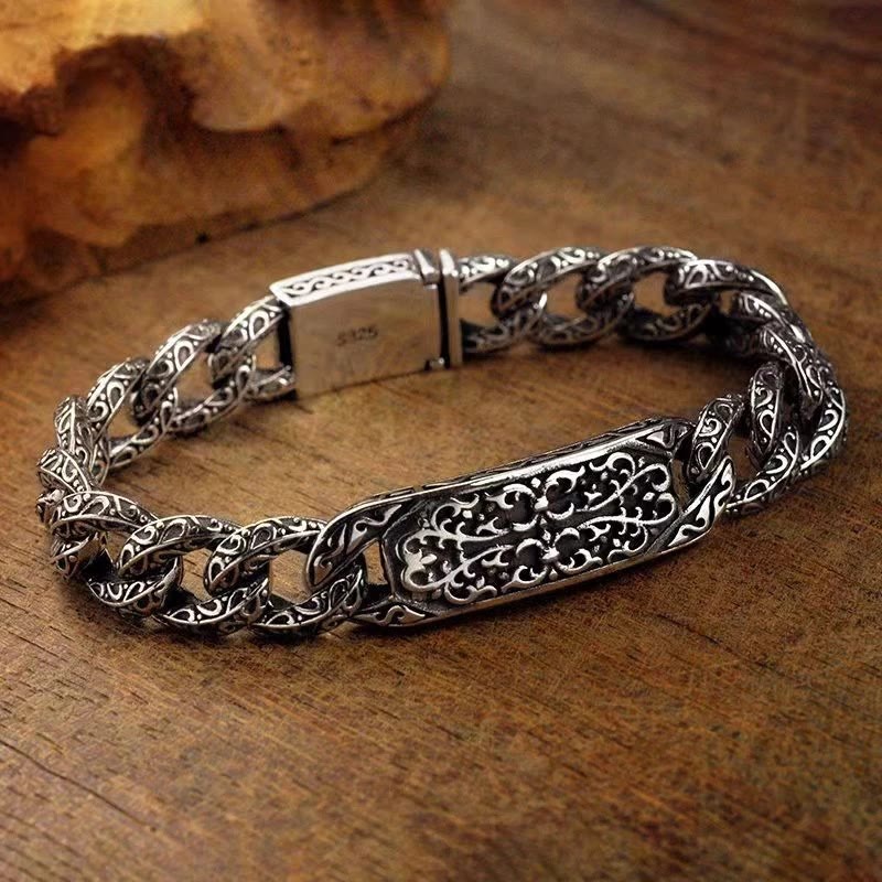 Silbernes Armband mit ornamentaler Gravur auf Holzoberfläche.