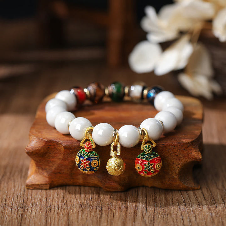Weißes Perlenarmband mit vergoldeten Glücksbringern auf Holz.