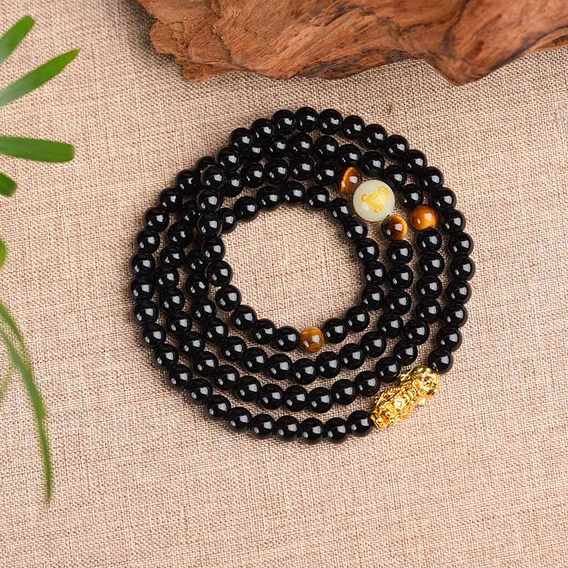 Schwarzes Obsidian Armband mit goldenen Akzenten auf Leinenstoff Untergrund